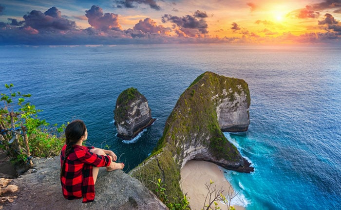 Woman sitting on cliff and looking at sunset at Kelingking Beach in Nusa penida island, Bali, Indonesia