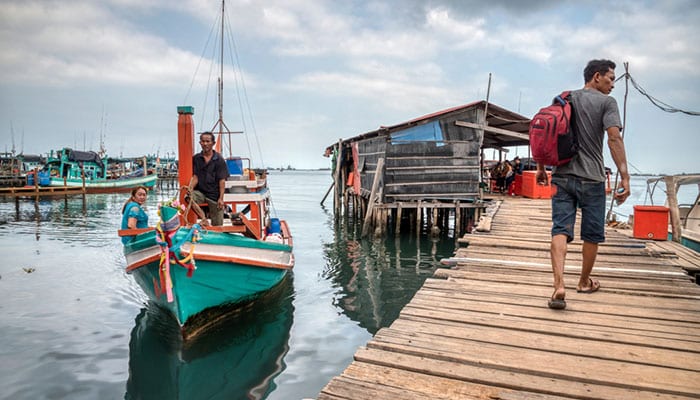 A man walking on the wooden jetty or pier 52 where local wooden boat among other boats along the Tomnub Rolork Road.