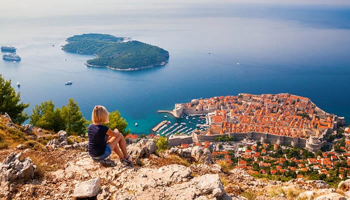 Young woman enjoying the view of the Dubrovnik Old Town, sitting on the mountain above the city